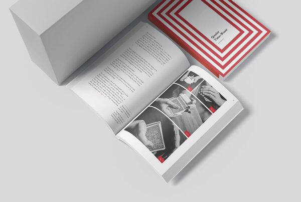 Open book showing black-and-white photos of card handling with a red-and-white striped box nearby, in a clean studio setup.