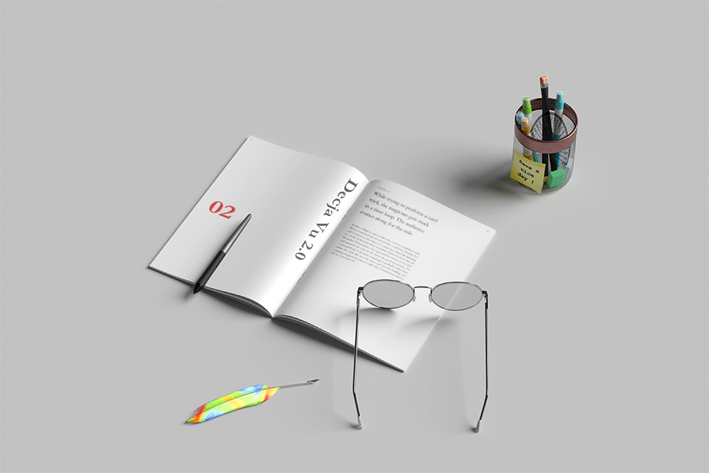 Open notebook with a pencil, colorful feather, and a pair of glasses on a gray desk, with a cup of pens and sticky notes nearby.